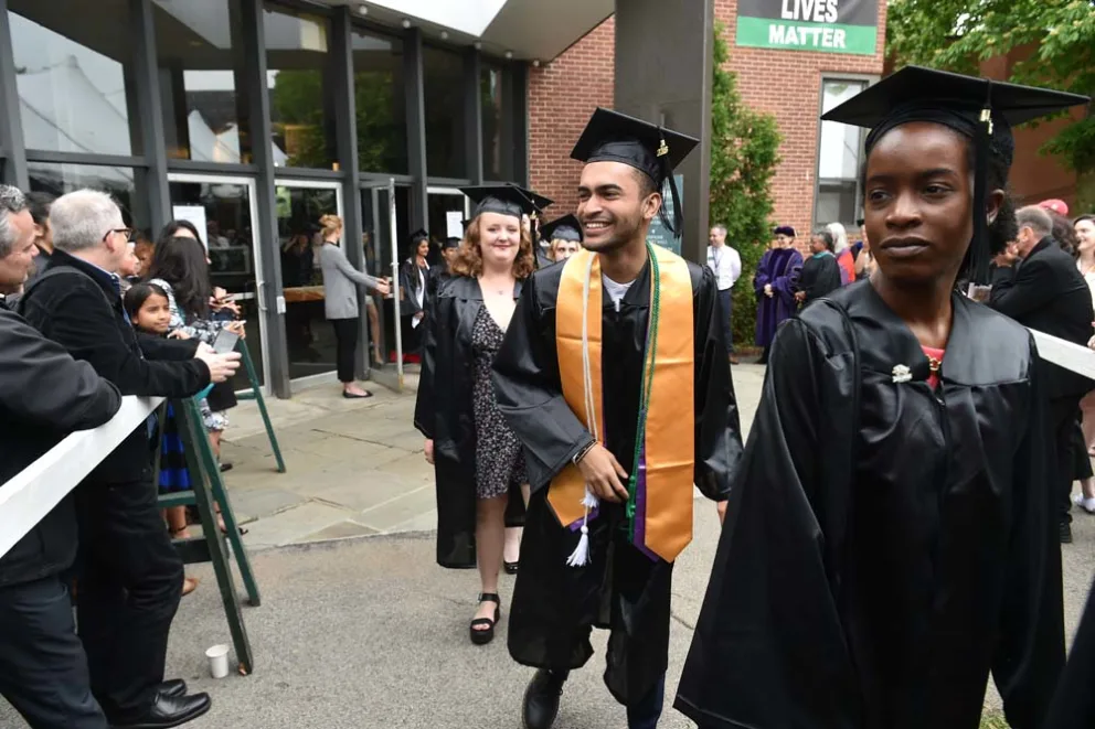 Graduates in caps and gowns celebrating commencement, with a "LIVES MATTER" banner in the background.
