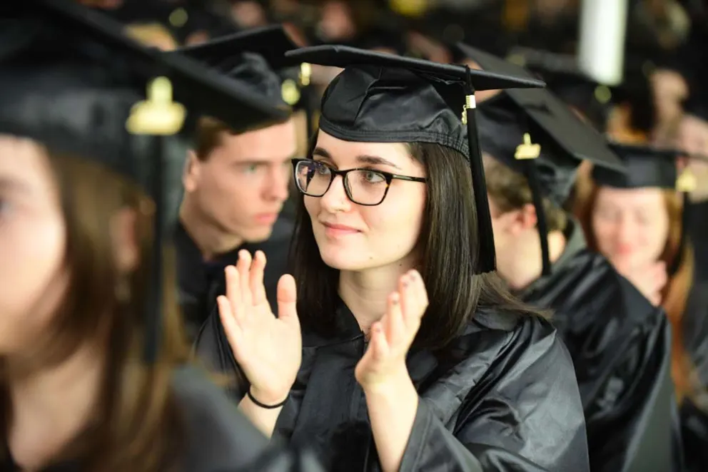 Individual in graduation cap and gown clapping among peers.