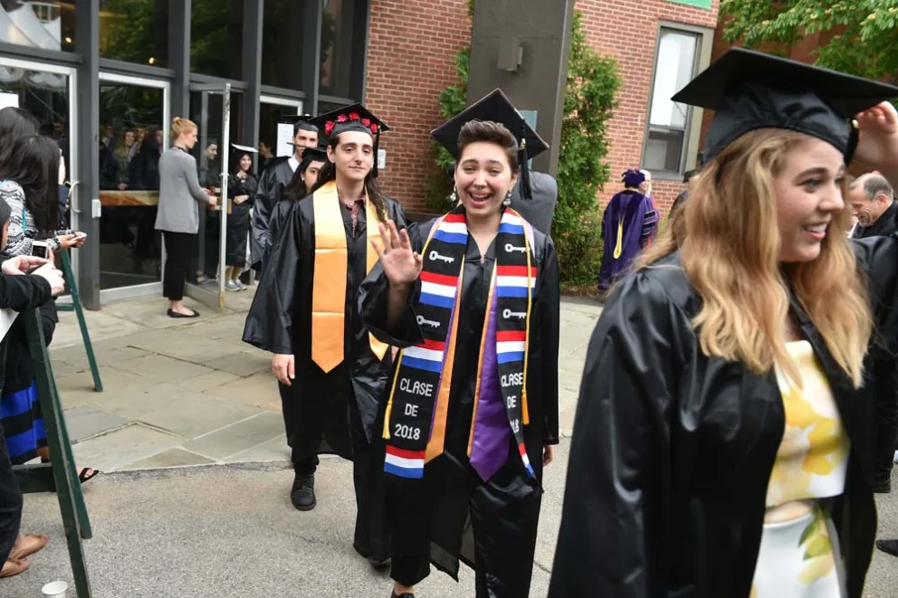 Graduates in caps and gowns celebrating, one waving, with stoles indicating 2018.