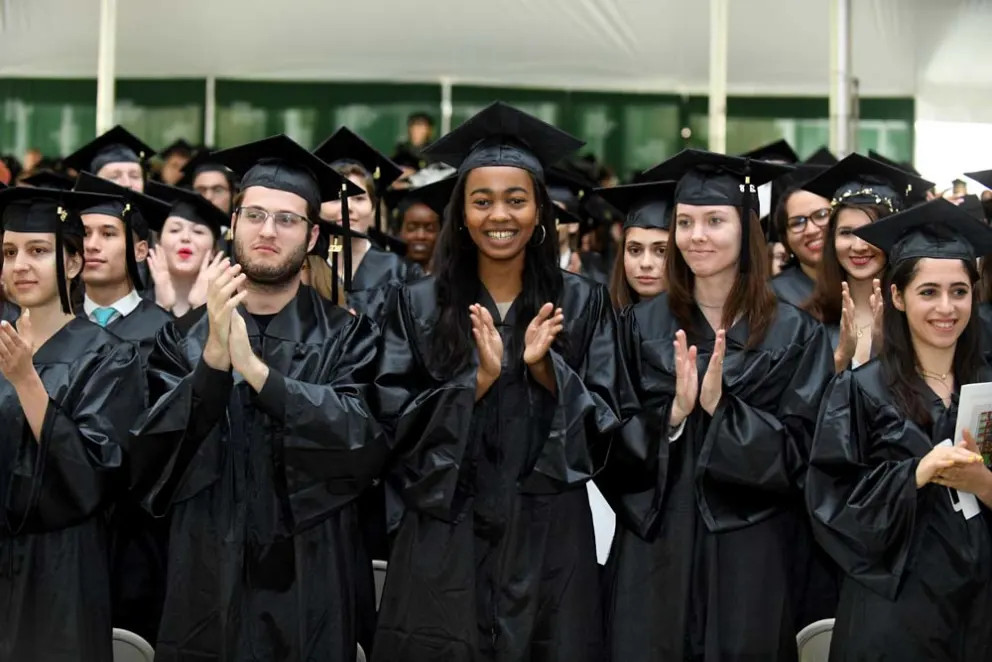 Graduates in caps and gowns clapping at a ceremony.