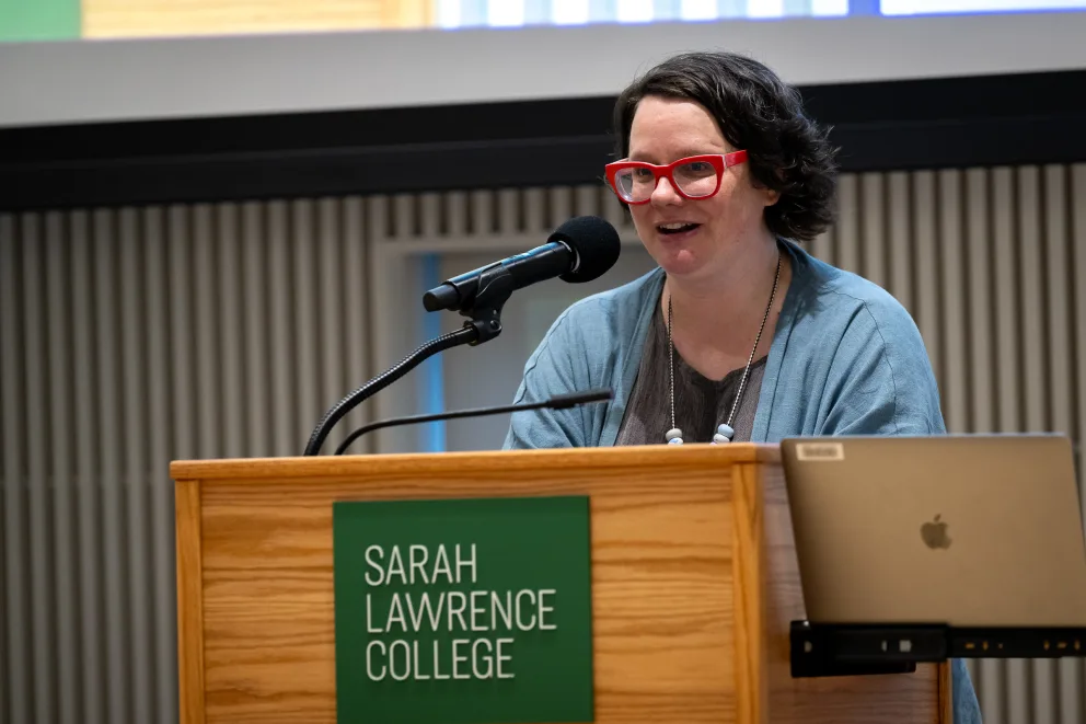 a woman in glasses speaking at a podium with a laptop on the side of the podium and a sign that says sarah law enforcement college