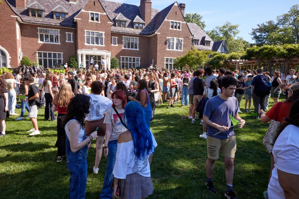 a large group of people standing in front of a building on a grass covered field in front of a crowd of people