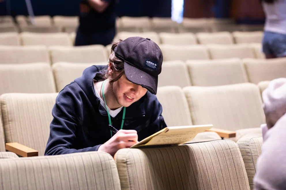 Student sitting auditorium seat writing notes