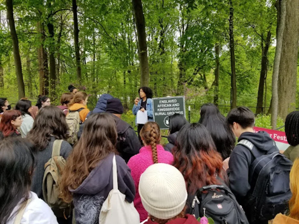 a group of people standing around each other in a forest with a sign on the side of the road