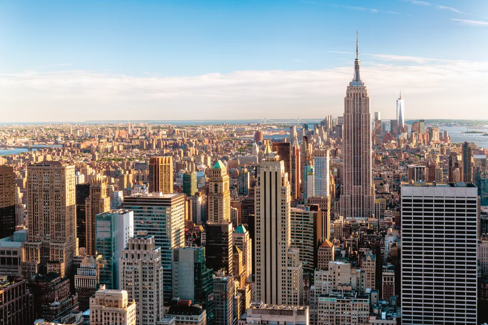 Aerial view of a city skyline with numerous skyscrapers, including a tall, iconic building, under a clear, blue sky.