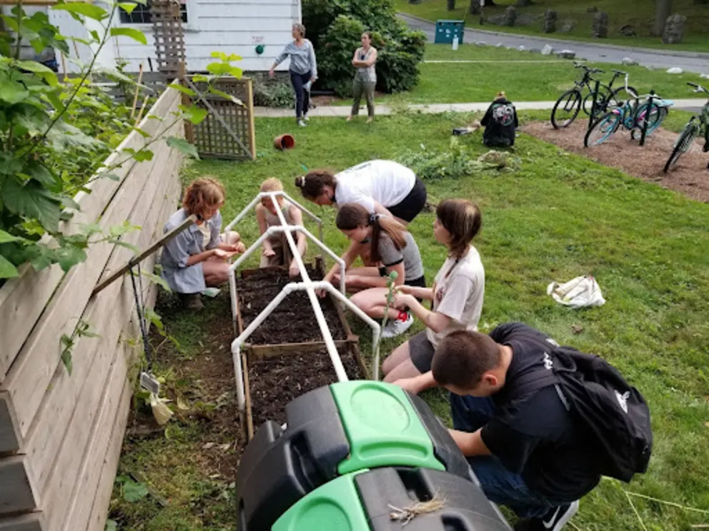 a group of people working in a garden with a wheelbarrow in the foreground and a green wheelbarrow in the background