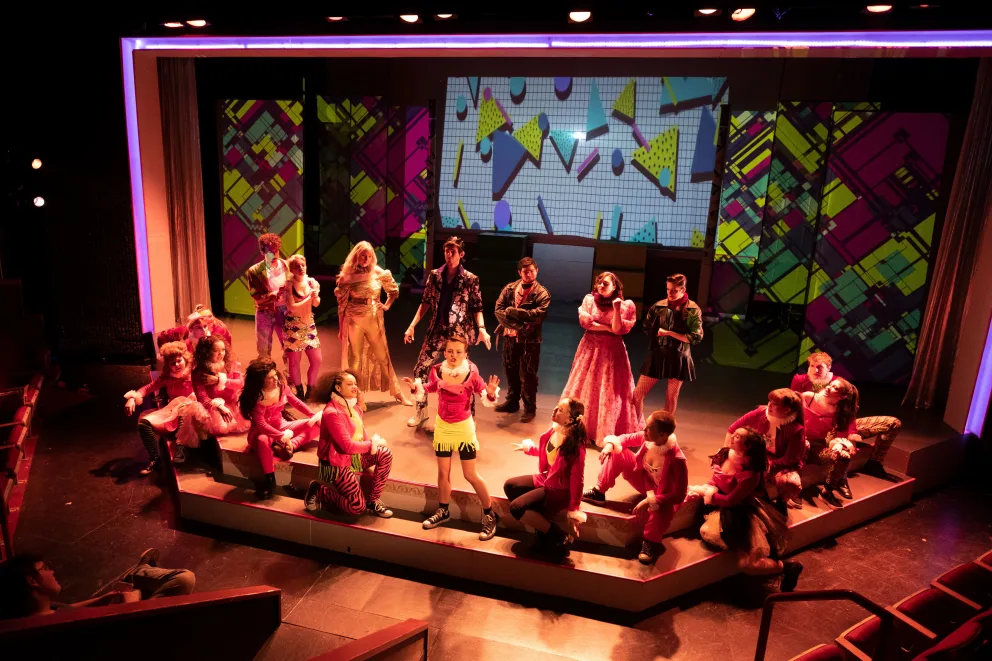 A group of people standing on top of a stage next to a crowd of people sitting on the floor.