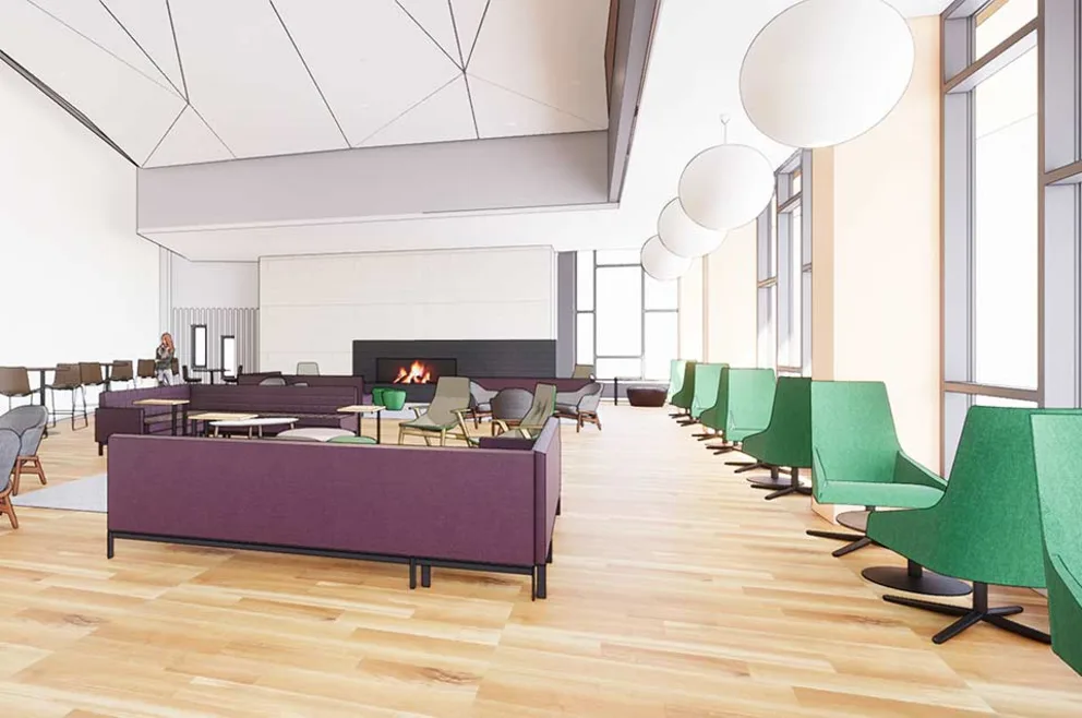 Spacious modern lounge with green and purple seating, wood floors, a fireplace, and large windows. A person sits at a table in the background.