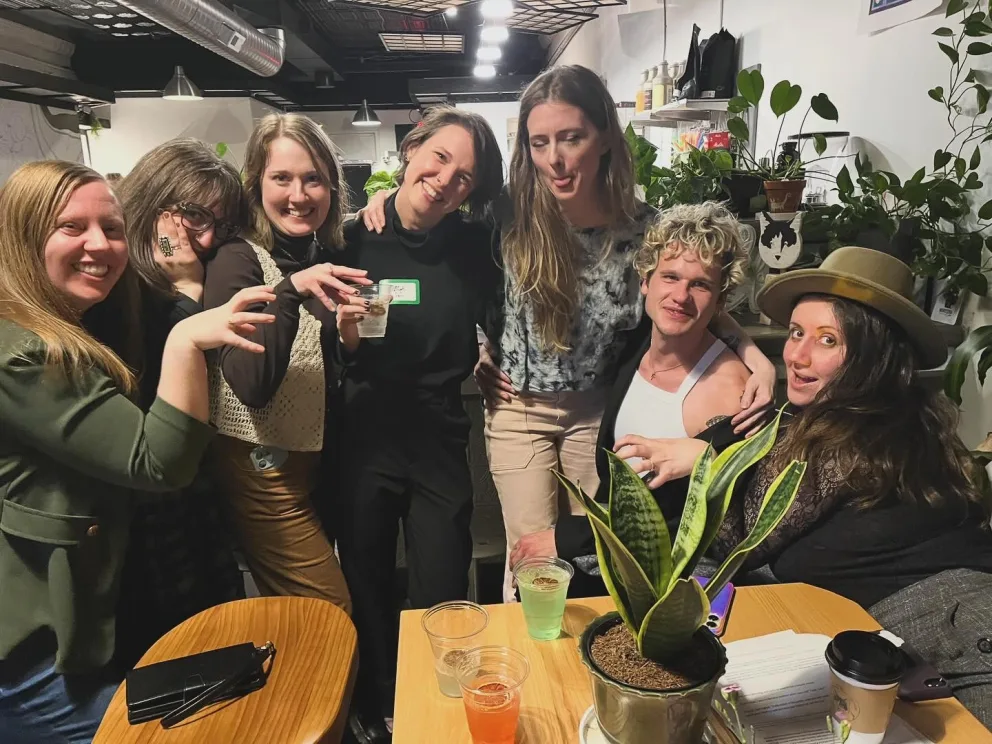 Group of individuals posing with drinks and plants in an indoor setting.