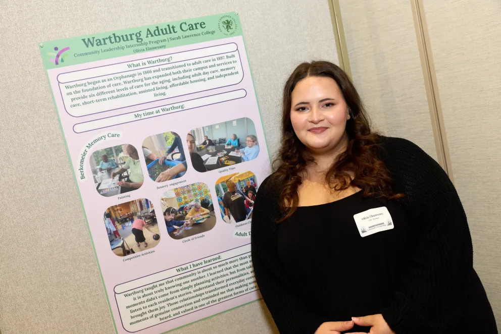Person smiling beside a presentation board titled "Wartburg Adult Care" with text and photos about care services and personal experiences.