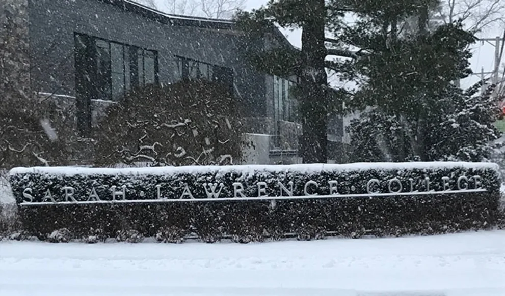Snow-covered Sarah Lawrence College sign with a modern building and trees in the background.