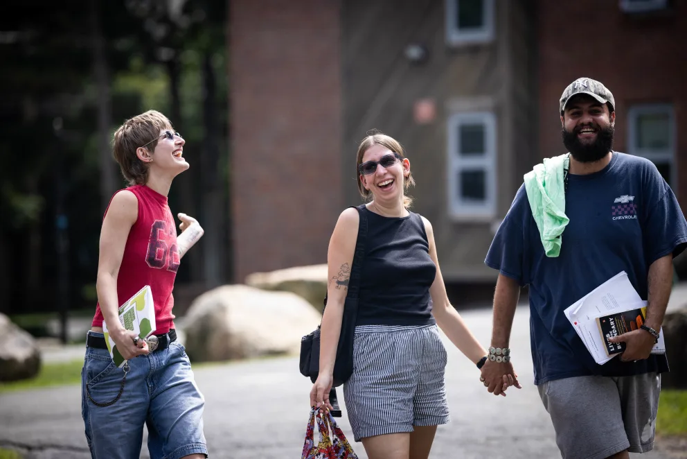Three people walking and laughing outside, holding hands, with buildings and rocks in the background.