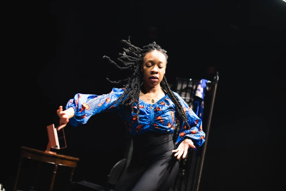 a woman standing on a stage with a chair in front of her and a chair in the back of the room behind her