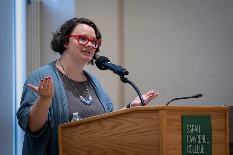 a woman standing at a podium with her hands up in front of her and a microphone in front of her
