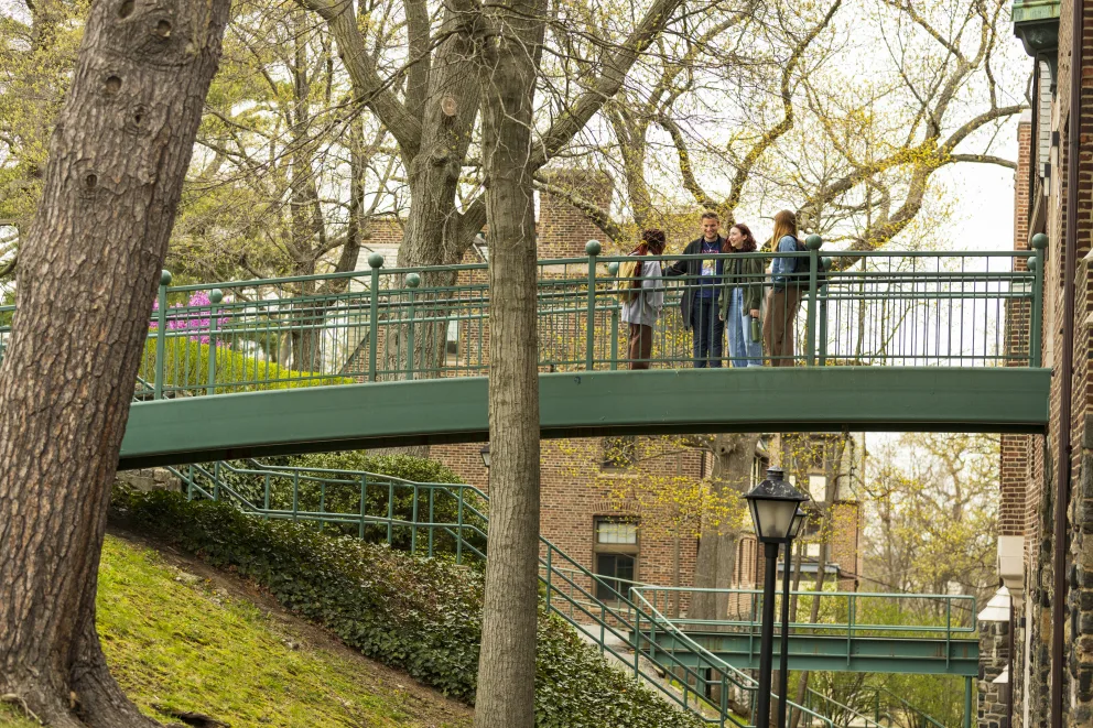 Four people standing on a green bridge surrounded by trees and buildings.