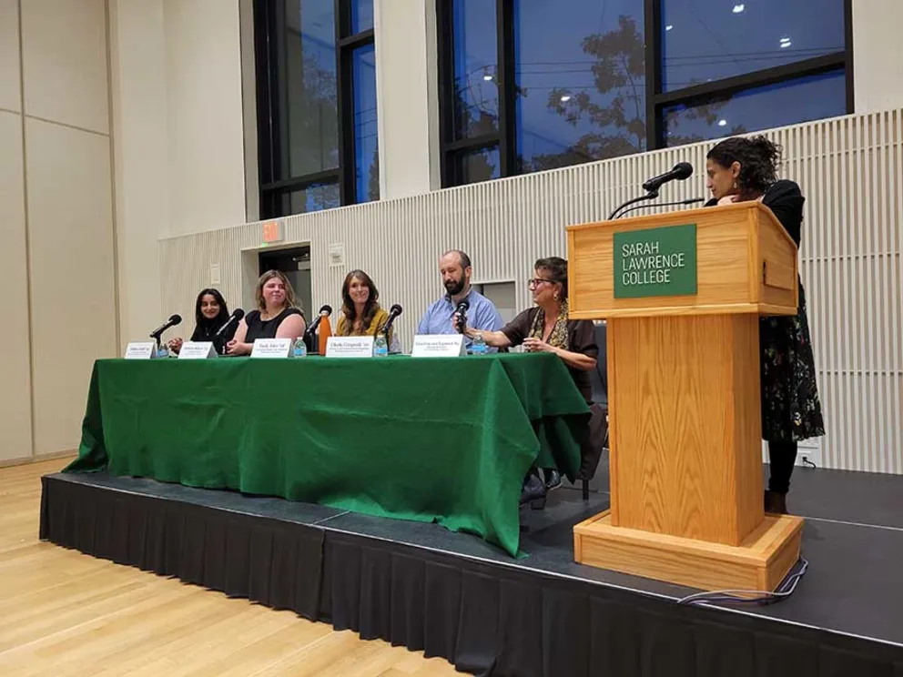 Five panelists sit behind a green table on a stage at Sarah Lawrence College, with a speaker at a podium to the right.