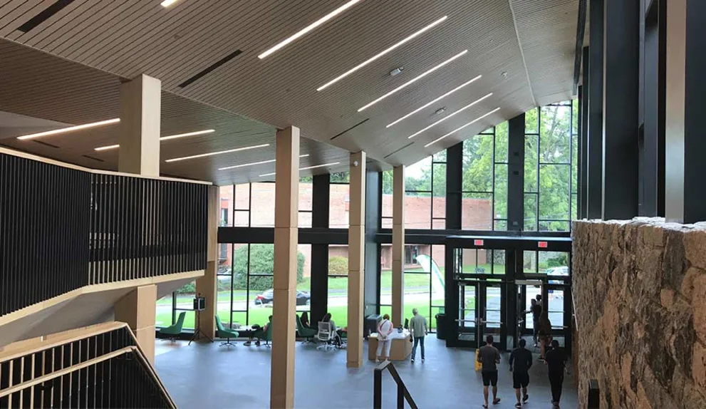 Spacious modern building lobby with high ceilings, large windows, stone wall, and several people walking towards the glass entrance.