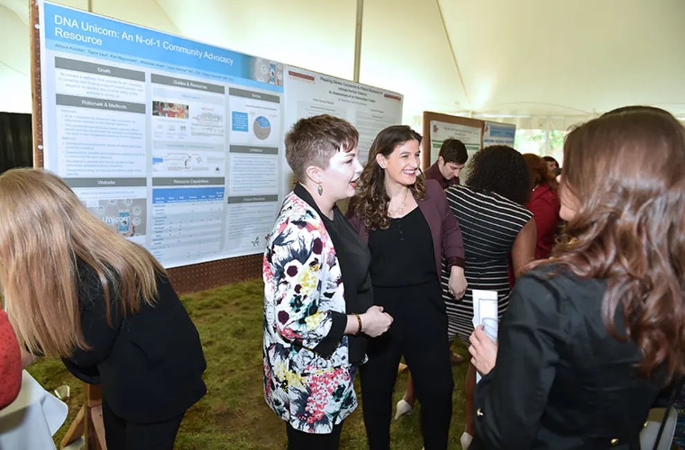 People in a tent converse in front of science posters titled "DNA Unicorn: An N-of-1 Community Advocacy Resource."