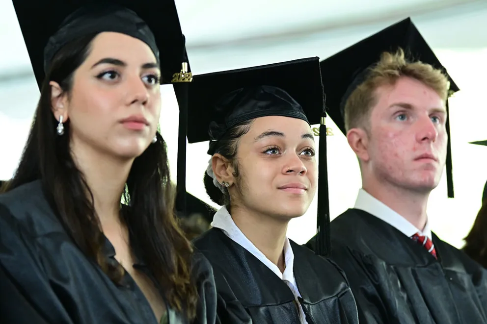 Three people in graduation caps and gowns sit attentively.