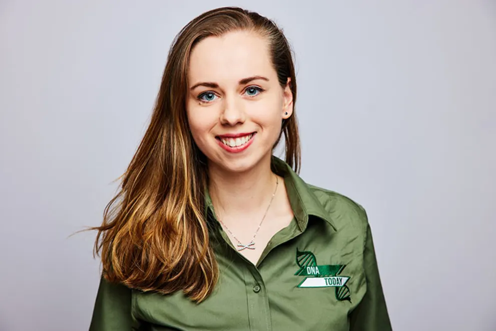 Person smiling with long hair, wearing a green shirt with "DNA Today" logo on it, against a plain background.