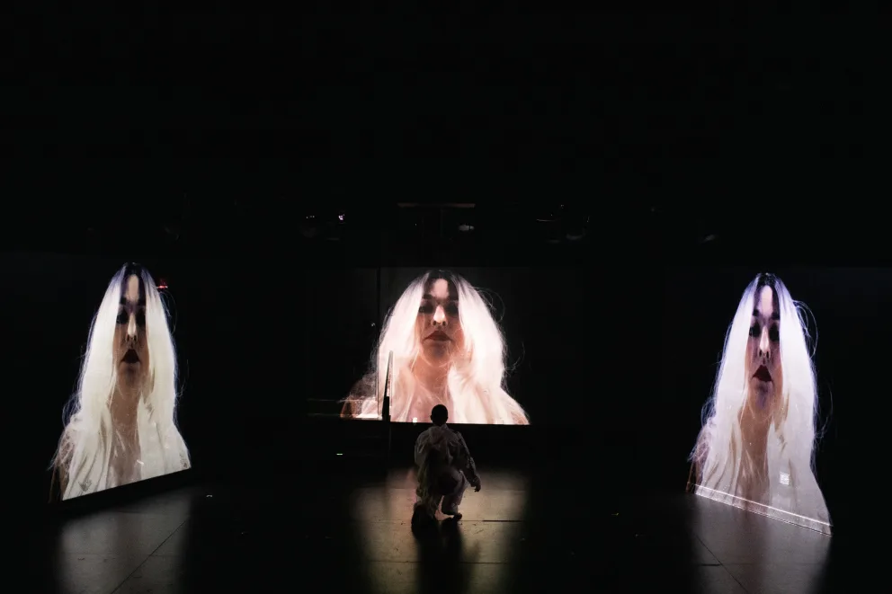 a woman with long white hair is standing in front of a screen with her hair blowing in the wind