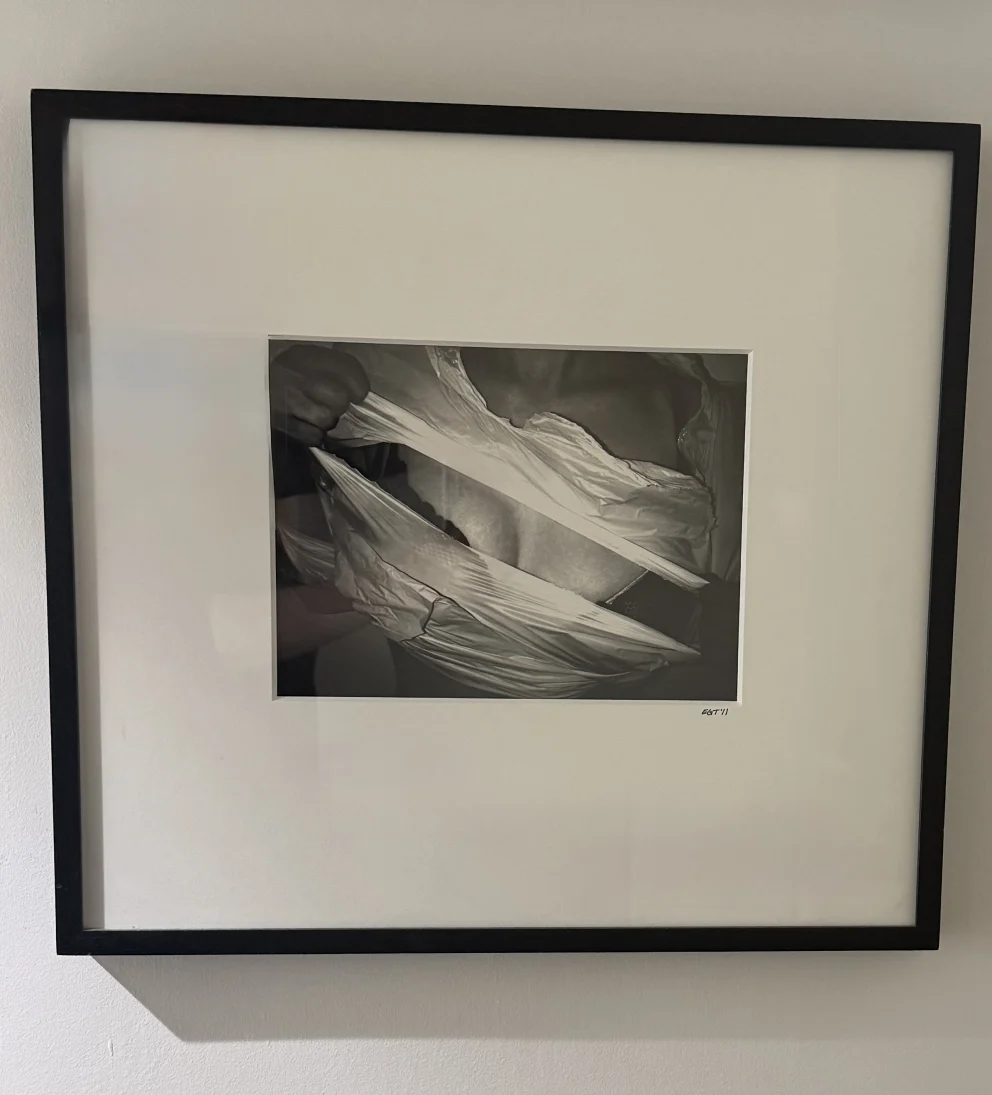 Framed black-and-white photograph of fabric being pulled apart, forming dynamic creases and shadows.