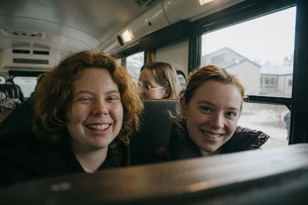 a couple of women sitting on top of a bus next to each other in front of a large window