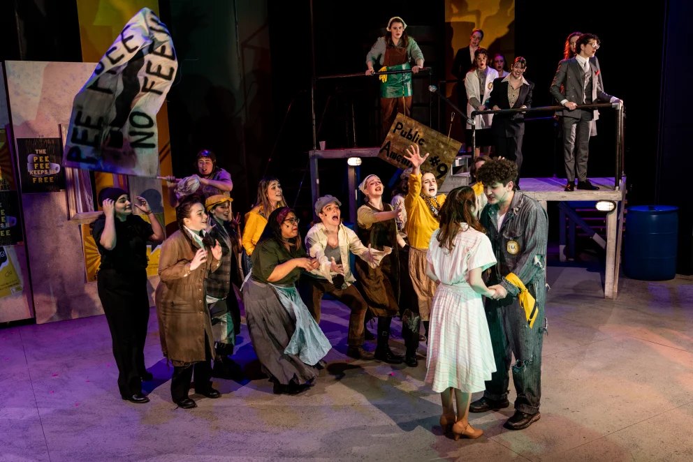 a group of people standing on top of a stage next to a crowd of people wearing costumes and holding signs