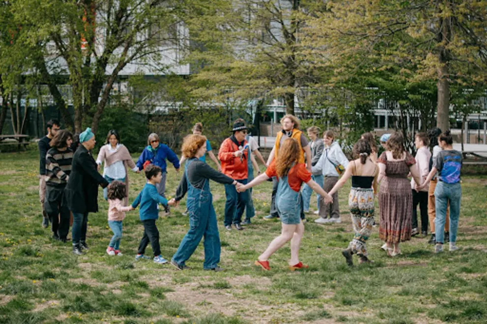 A group of people is gathered in a park, with a man and a woman dancing together.