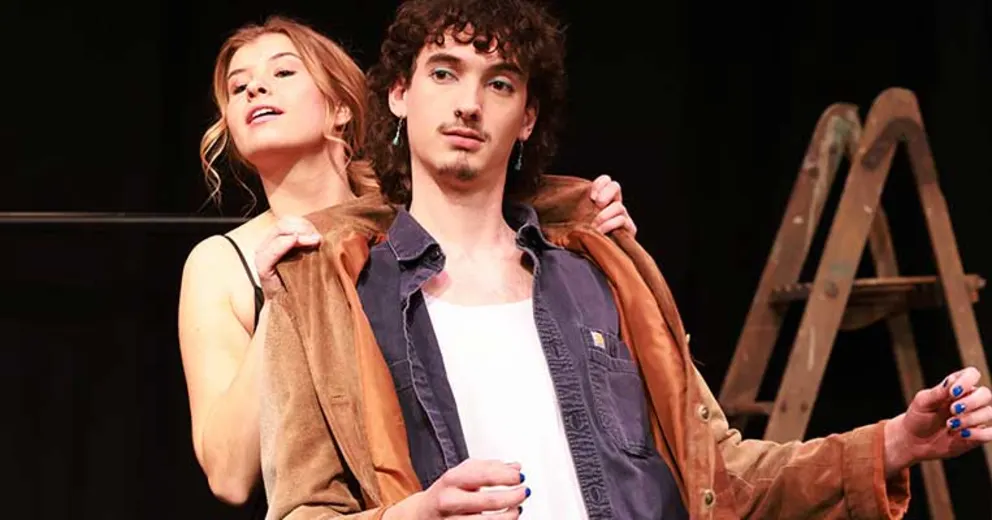 Two people pose together, one wearing a jacket. A ladder is visible in the background.