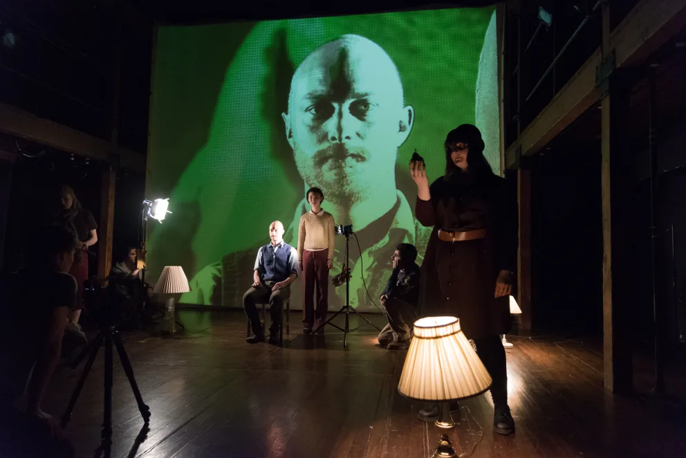 a group of people standing in front of a large screen with a picture of a man on it and a lamp in front of them