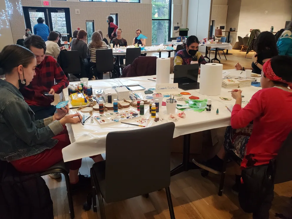 a group of people sitting at a table with paint and paper on it in front of a large window