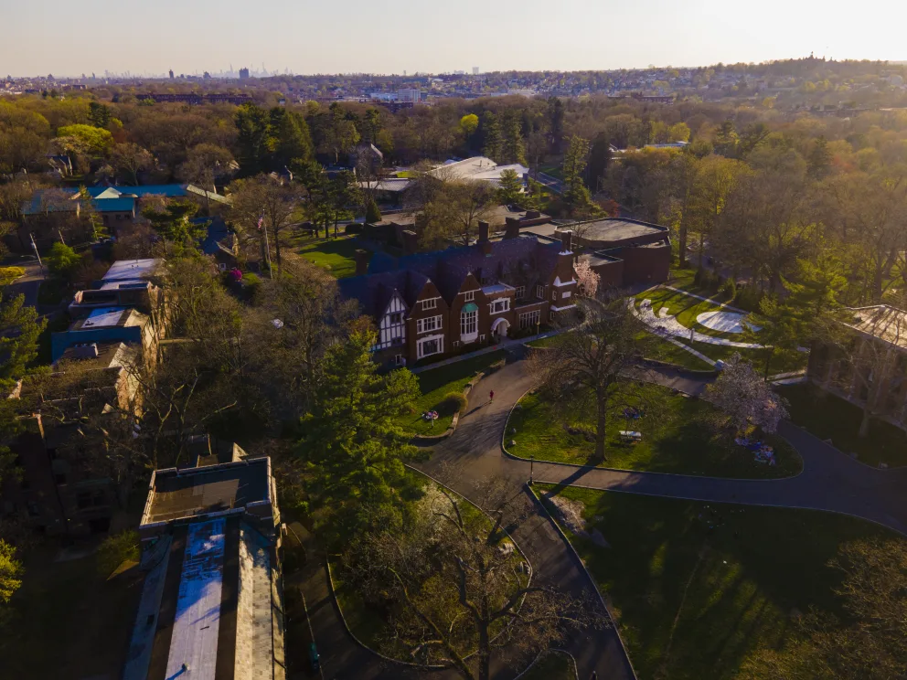 Aerial view of a large estate with a grand building surrounded by trees and pathways, set in a broad, park-like landscape at sunset.