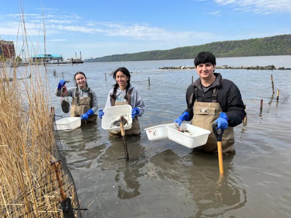 a group of people standing in the water with buckets of food in their hands and a man holding a shovel
