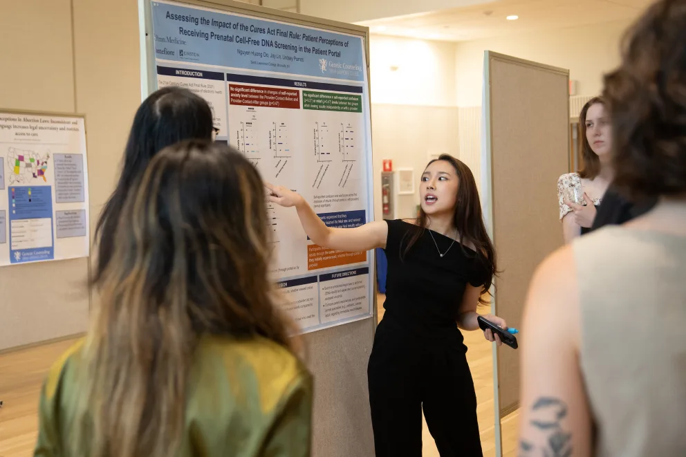 A person presents research on a poster to a small group in a well-lit room.