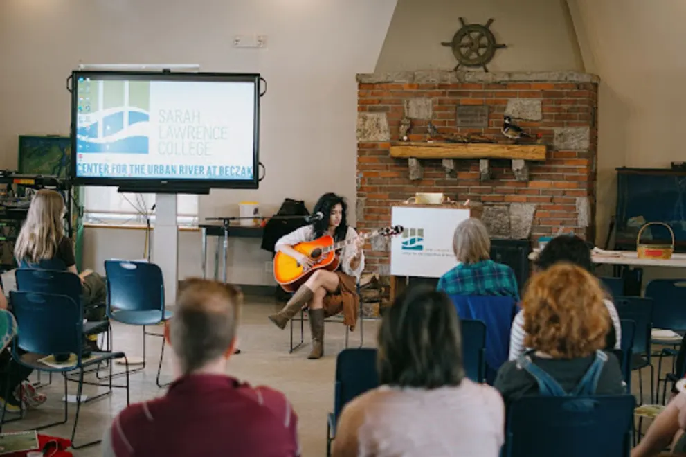 a group of people sitting in chairs watching a woman play a guitar in front of a crowd of people