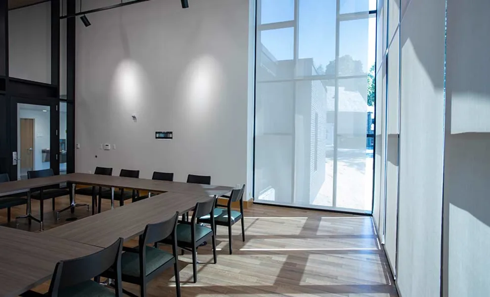 Conference room with a U-shaped table, several chairs, and large windows allowing natural light.