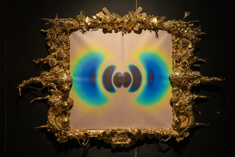 Ornate frame with gold decorations surrounds an abstract image featuring symmetrical blue and yellow patterns on a light background.