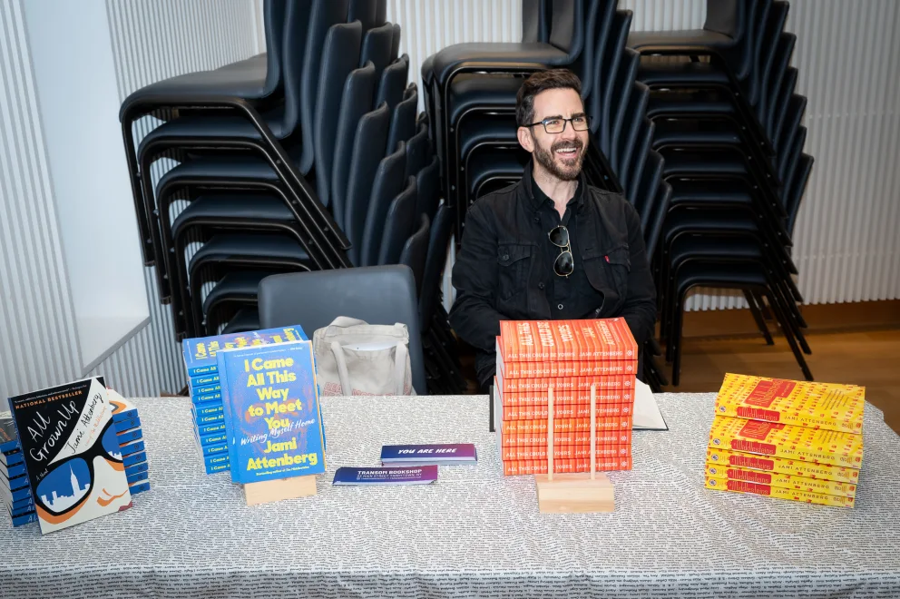 a man sitting at a table with a bunch of boxes on it and a stack of chairs behind him