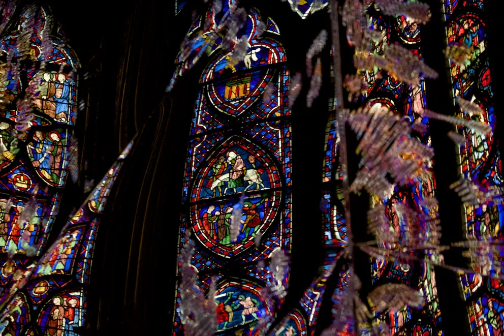Vibrant stained glass windows with intricate patterns and figures, surrounded by colorful reflections in a dimly lit setting.