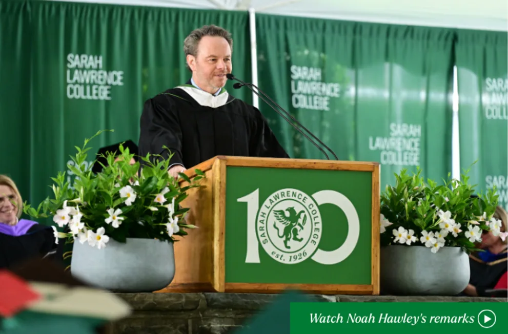 Person in academic attire speaks at a podium with "Sarah Lawrence College" and floral decorations.