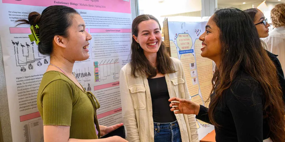 Three people engaged in conversation in front of science posters at a presentation event.