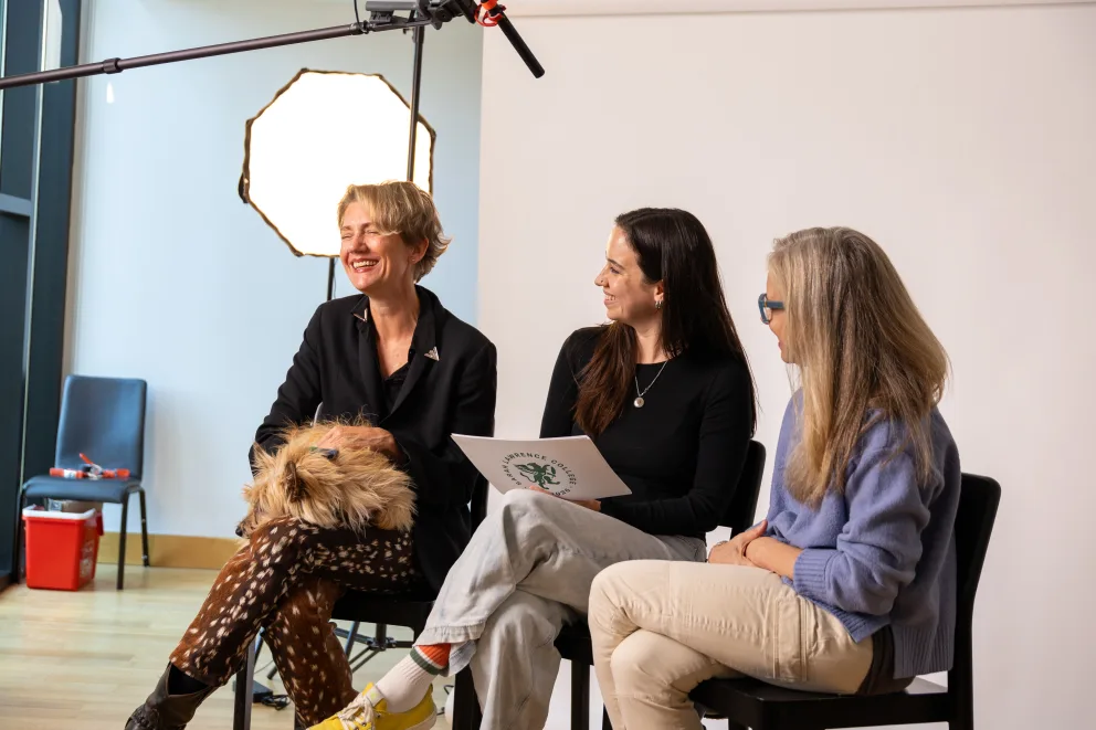 Three people sitting and smiling during a casual interview setup in a studio, with a fluffy dog in one person's lap.
