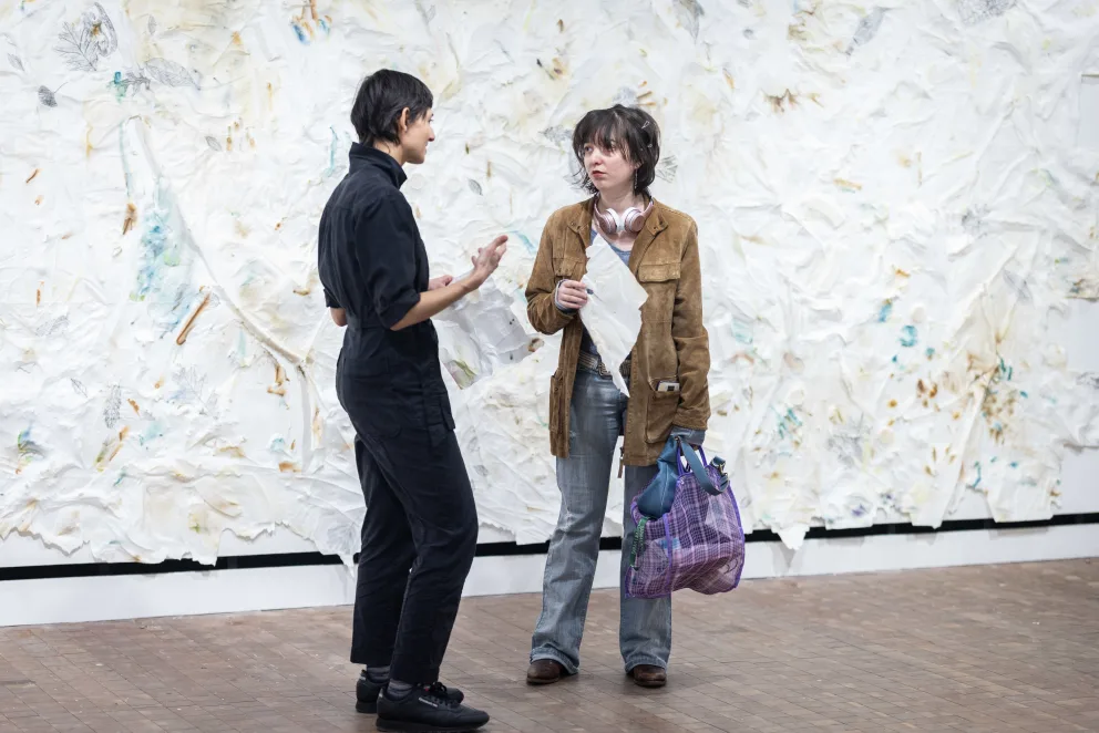 Two people are standing next to a large painting, one of them is pointing at it, and they are both holding cell phones.
