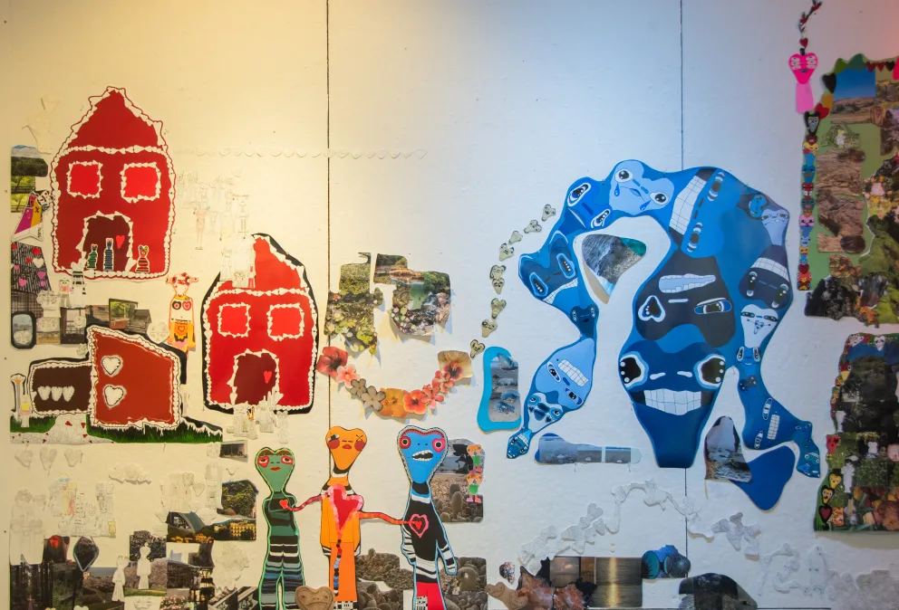 Colorful abstract artwork with red house shapes, three multi-colored figures with hearts, and a blue creature with faces against a textured background.