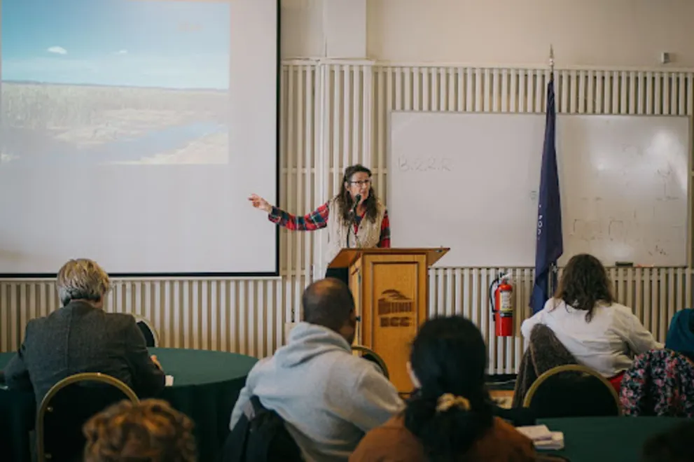 a woman standing at a podium in front of a group of people in front of a projector screen