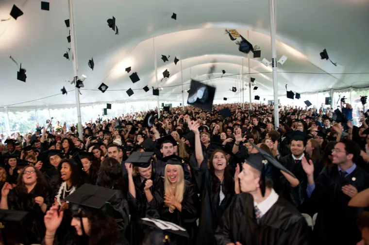 Graduates tossing caps in the air under a large tent.