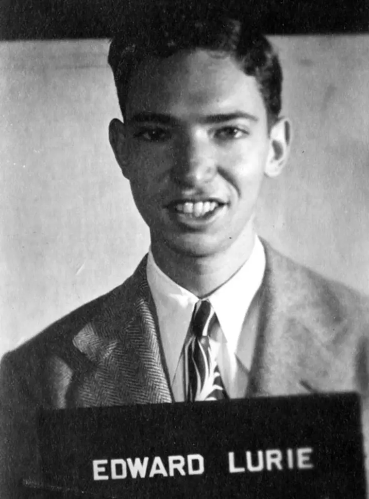 Person smiling in suit with 'EDWARD LURIE' sign. Black and white photo.