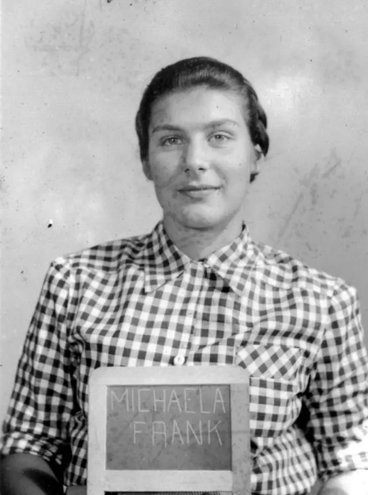 Person in checkered shirt holding a sign with a name on it, vintage black and white photo.