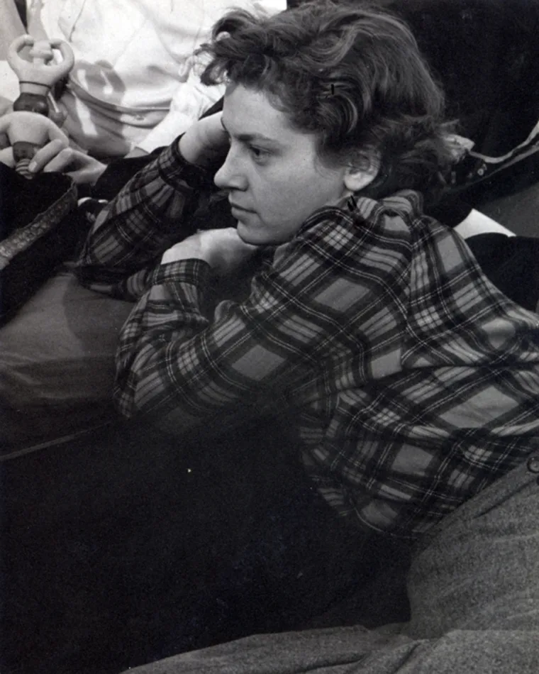 Individual in plaid shirt rests head on hand with contemplative expression.